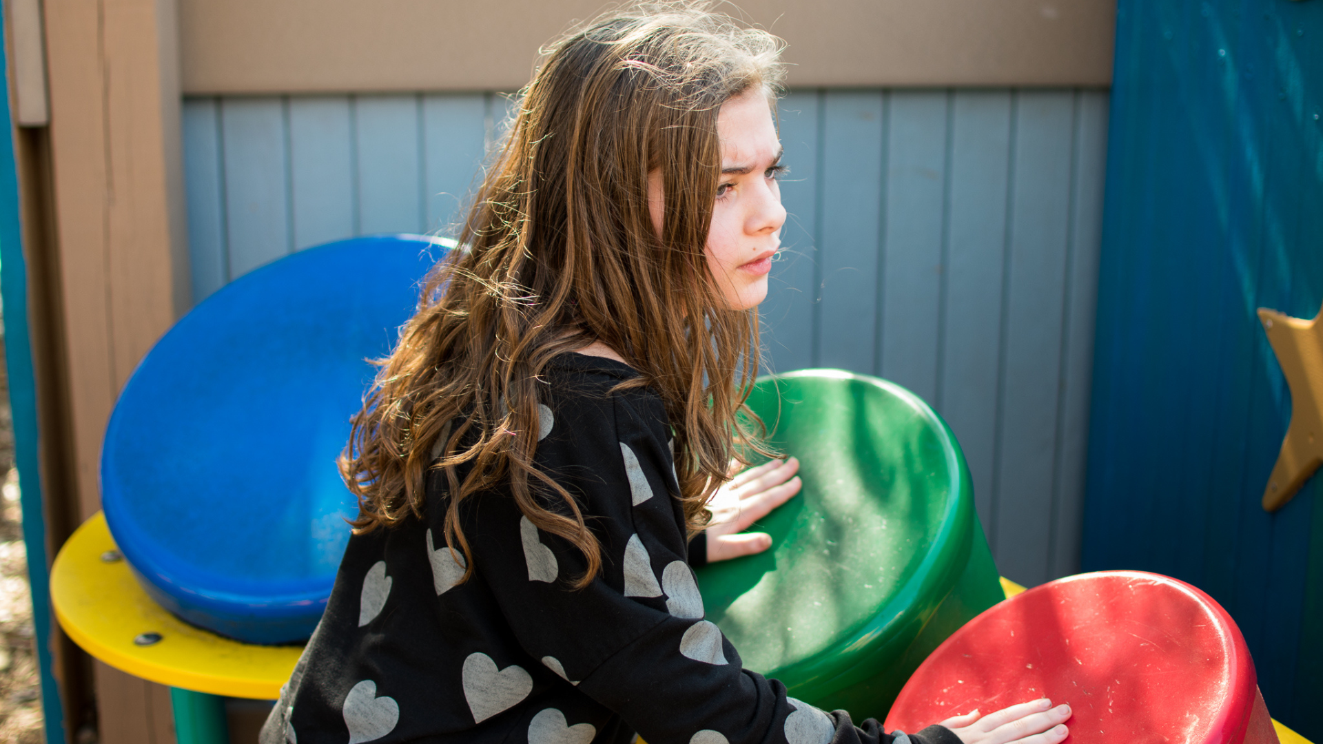 a girl with long hair and a black shirt with white hearts on it playing drums at Perdido Kids Park