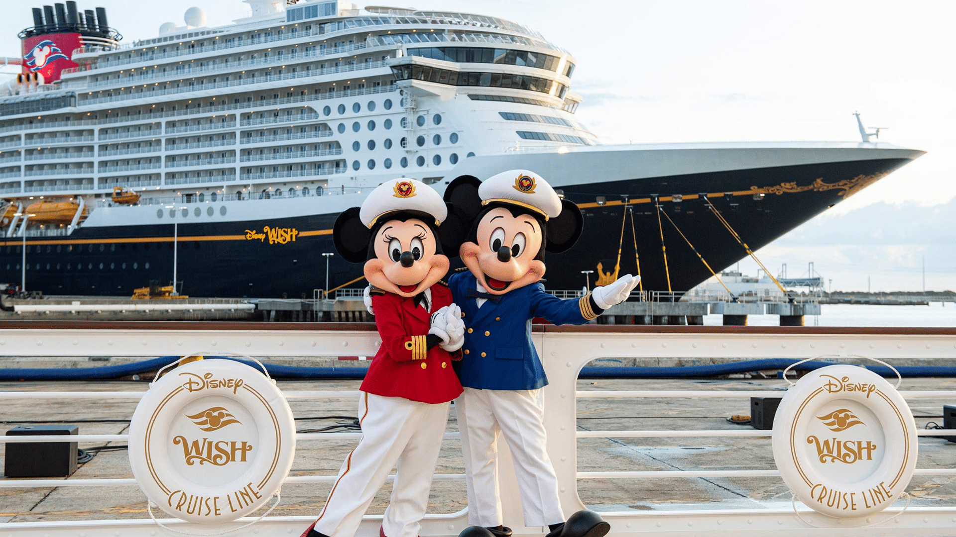 Captain Mickey and Captain Minnie standing in front of the Disney Wish